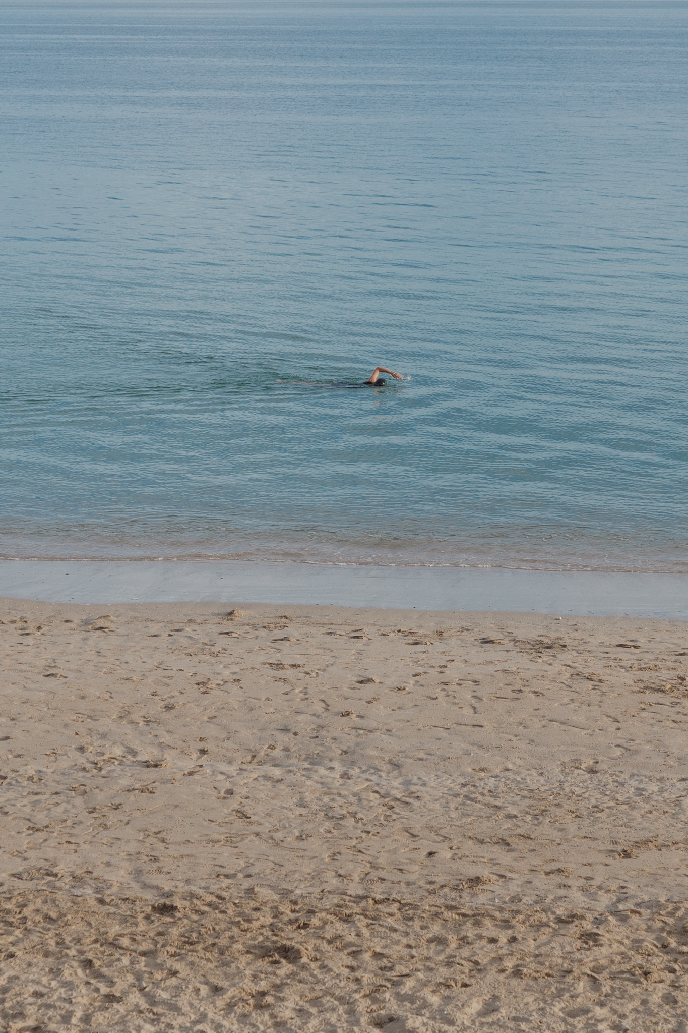 A person swimming in the sea near a sandy beach.